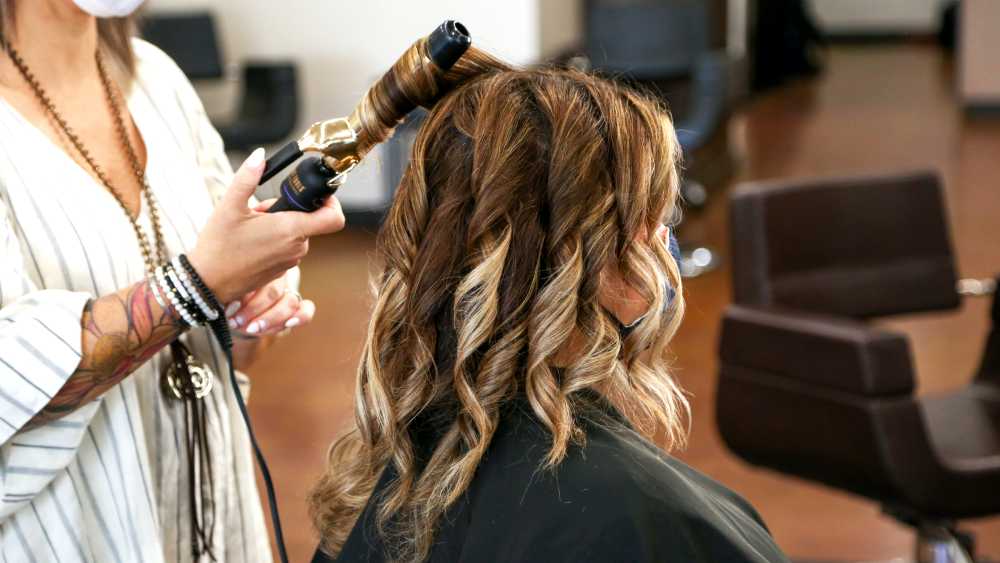 stylist curling client's hair with curling iron